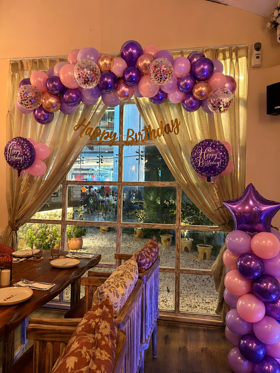 Restaurant celebration purple, pink and rose chrome balloon arch with confetti balloons and Happy Birthday cursive banner